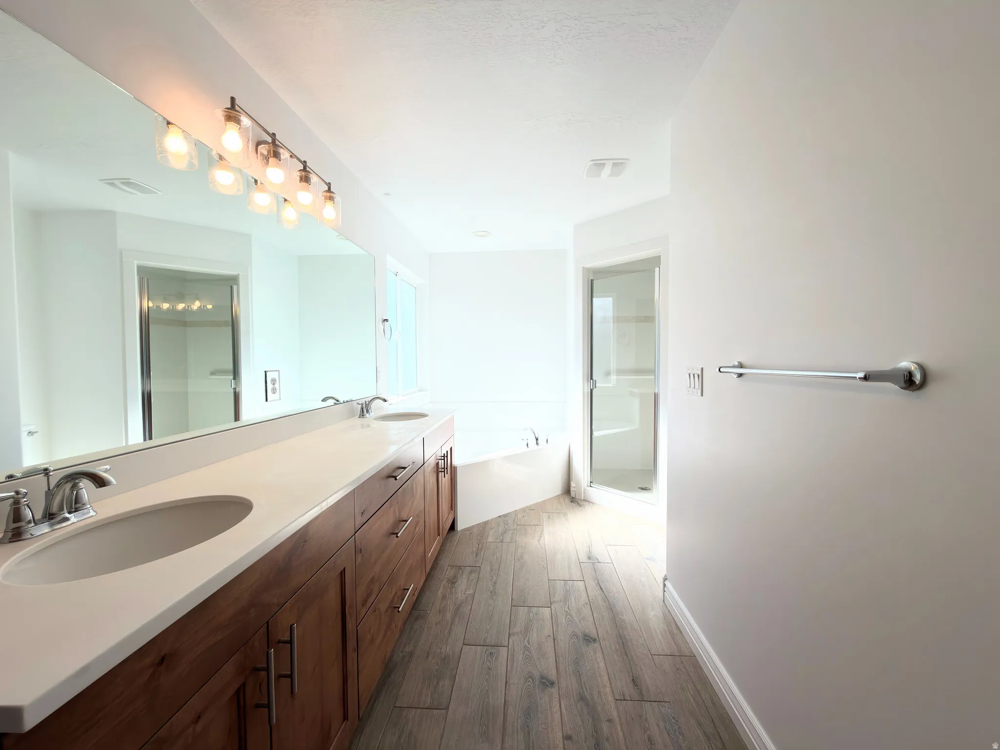 Bathroom featuring double vanity, dark wood finished floors, a garden tub, and a stall shower