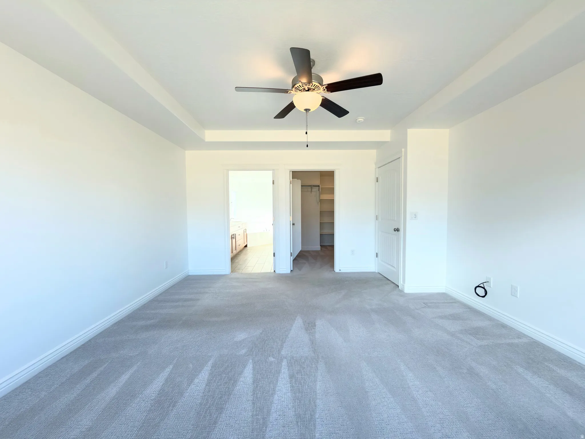 Unfurnished bedroom featuring connected bathroom, a spacious closet, carpet floors, a ceiling fan, and a tray ceiling