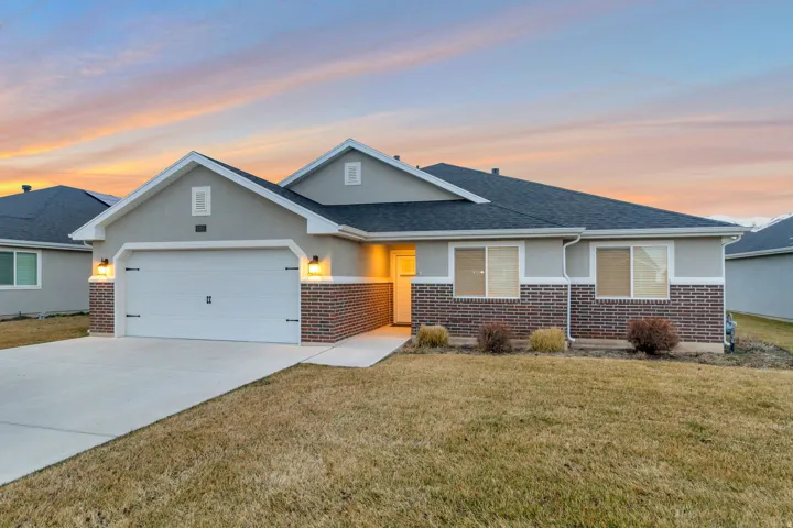 View of front of home featuring stucco siding, a yard, a garage, and brick siding