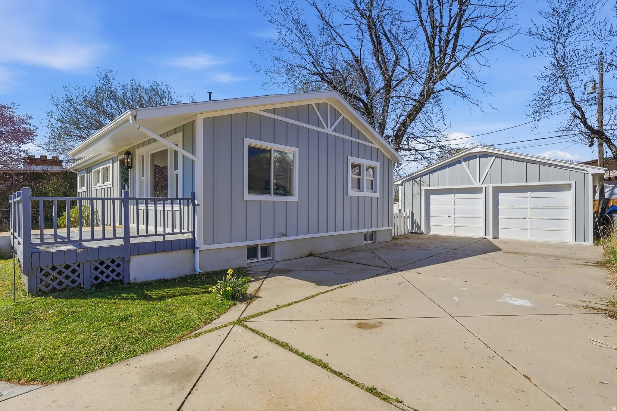 View of home's exterior with a detached garage, an outbuilding, board and batten siding, a deck, and a lawn