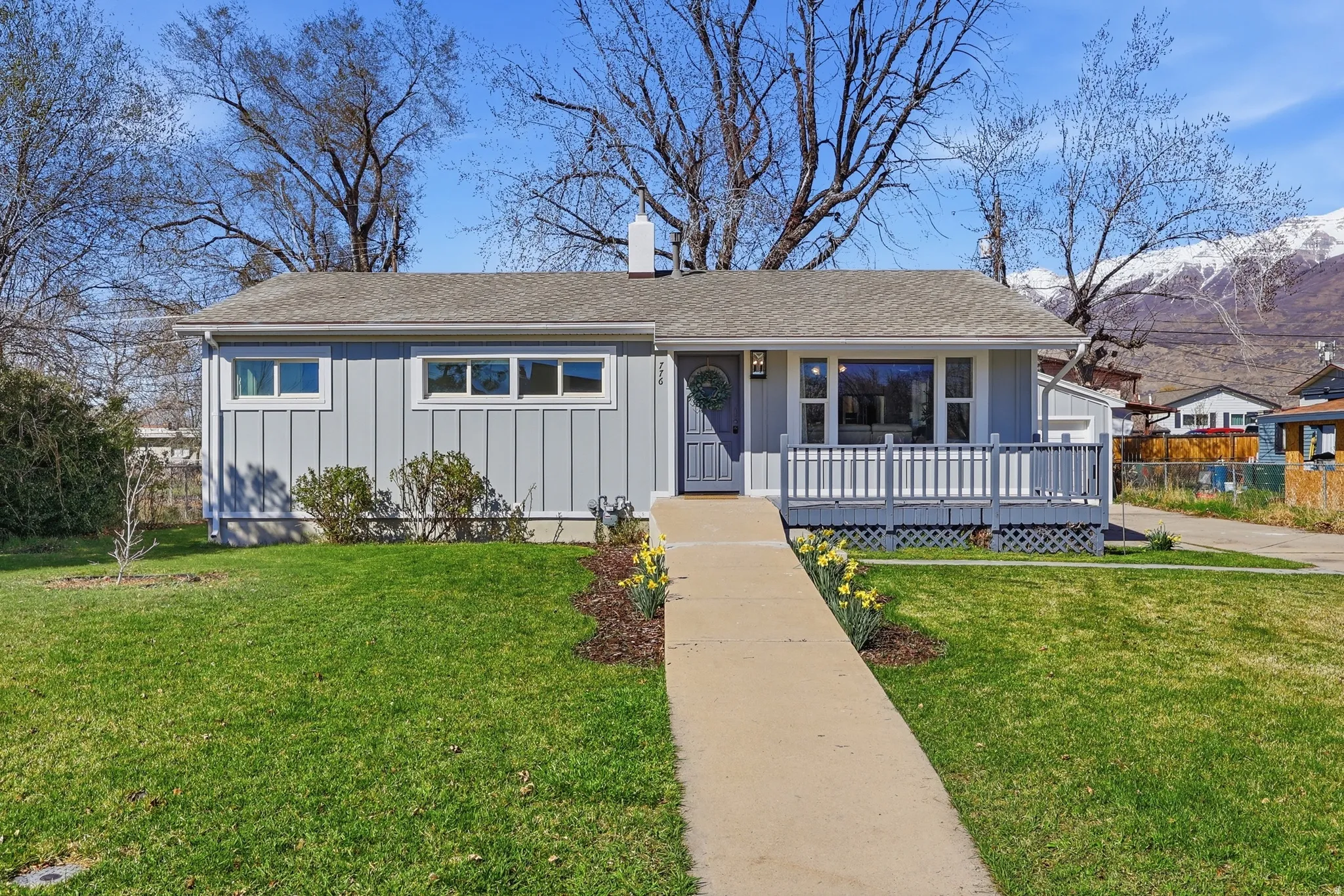 View of front of property with a front yard, covered porch, a shingled roof, board and batten siding, and a chimney