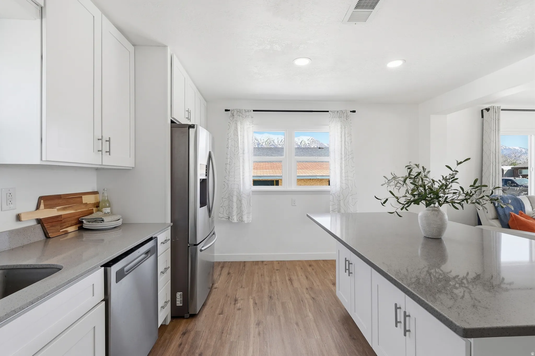Kitchen with white cabinetry, light stone counters, stainless steel appliances, light wood-type flooring, and healthy amount of natural light