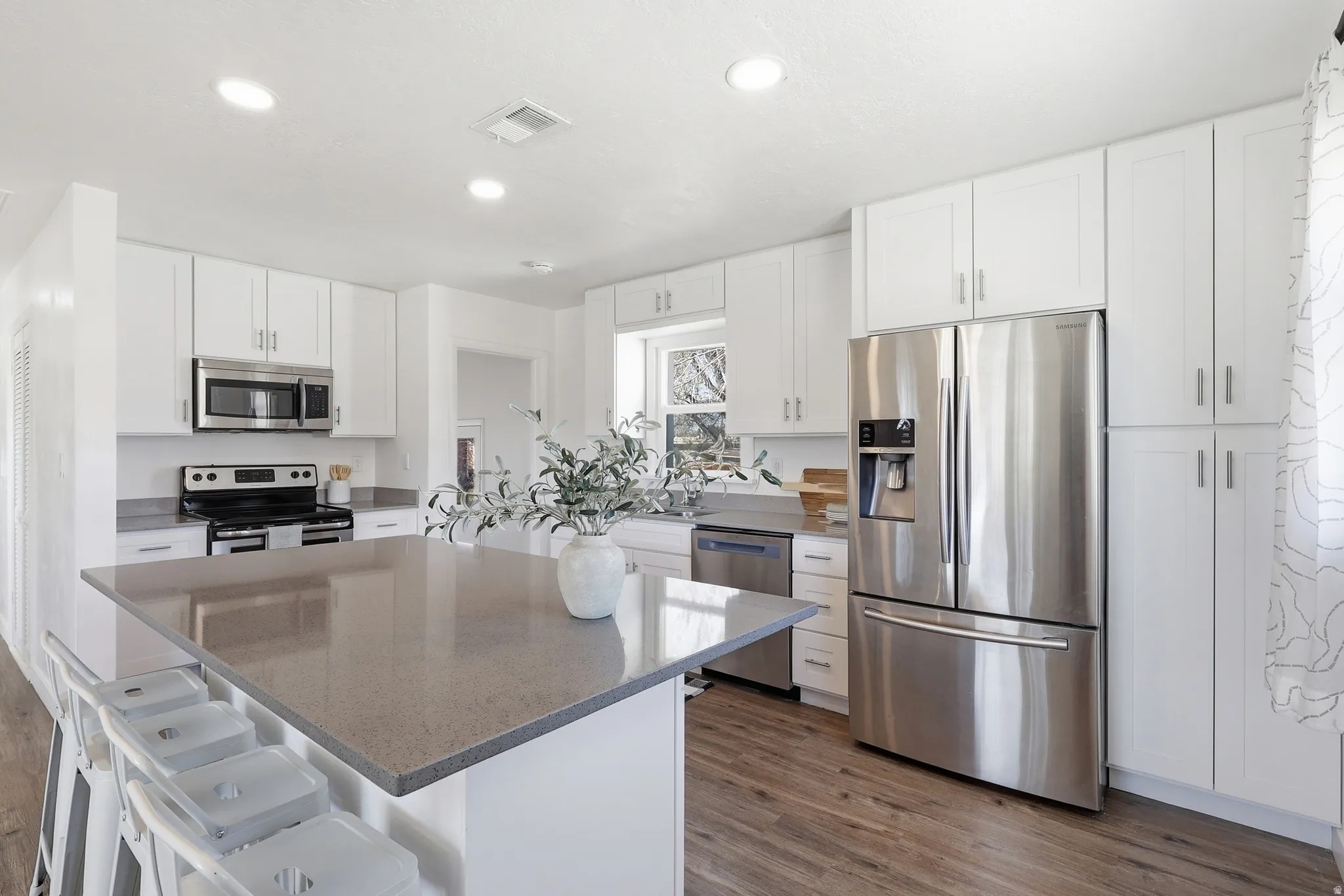 Kitchen featuring a breakfast bar area, stainless steel appliances, white cabinetry, a center island, and dark wood-type flooring