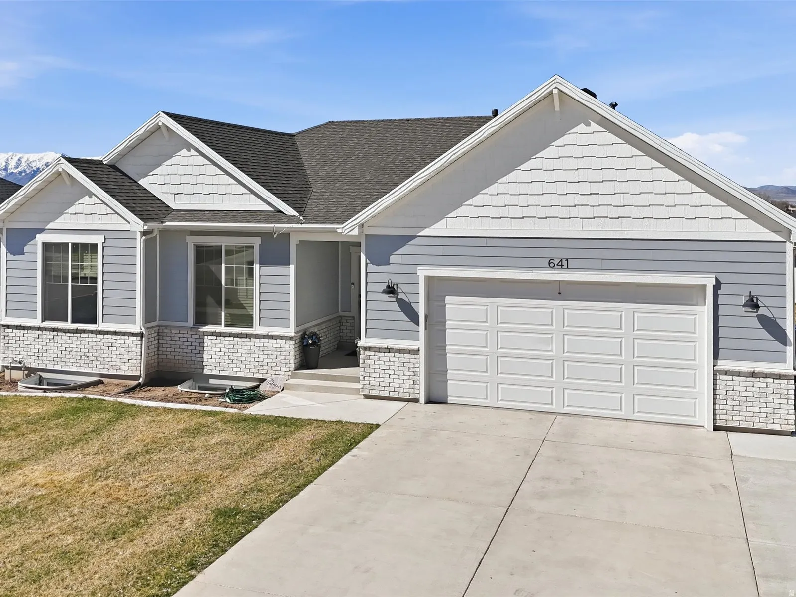 Craftsman house with a front lawn, driveway, an attached garage, brick siding, and roof with shingles