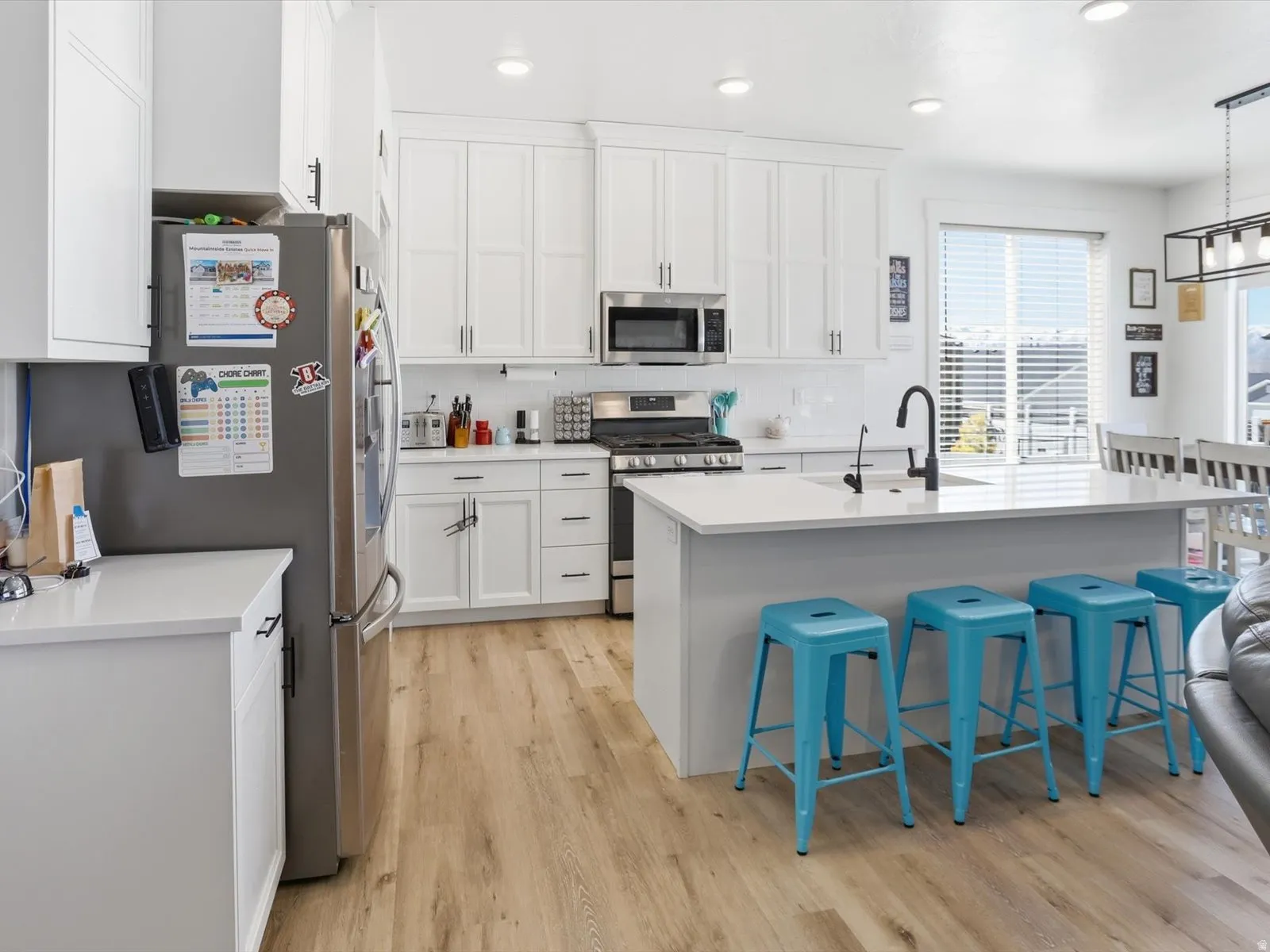 Kitchen with a kitchen breakfast bar, stainless steel appliances, white cabinets, an island with sink, and light wood-style floors