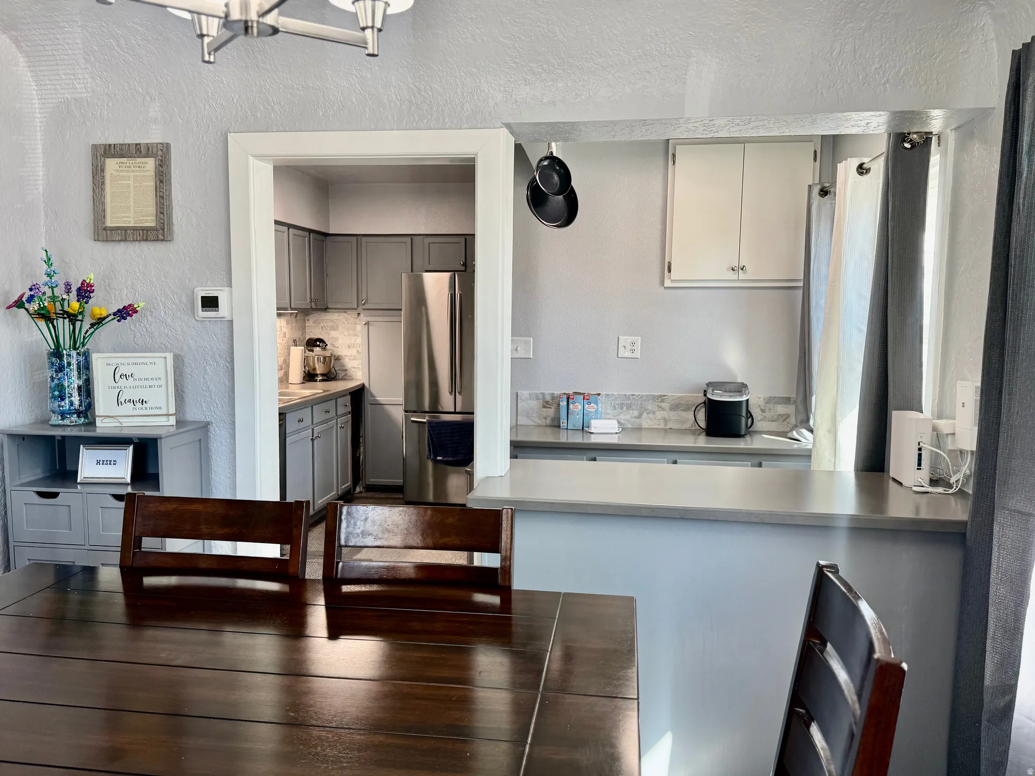 Kitchen with a textured wall, freestanding refrigerator, a peninsula, decorative backsplash, and gray cabinetry
