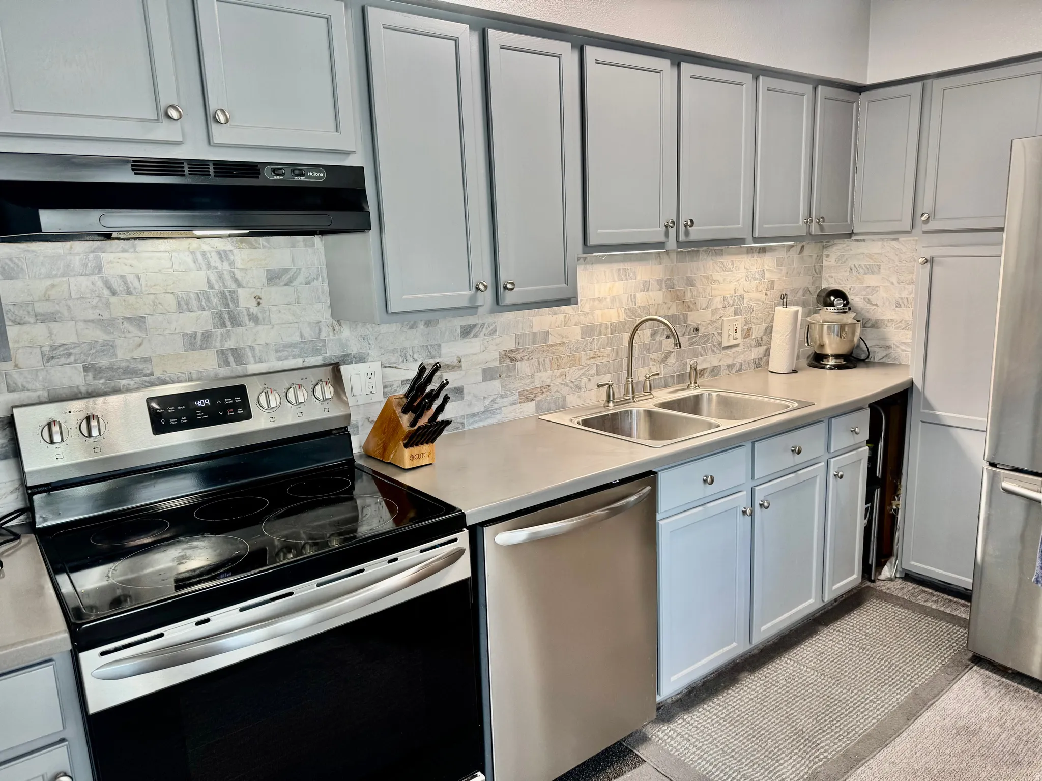 Kitchen featuring stainless steel appliances, light countertops, decorative backsplash, and gray cabinetry