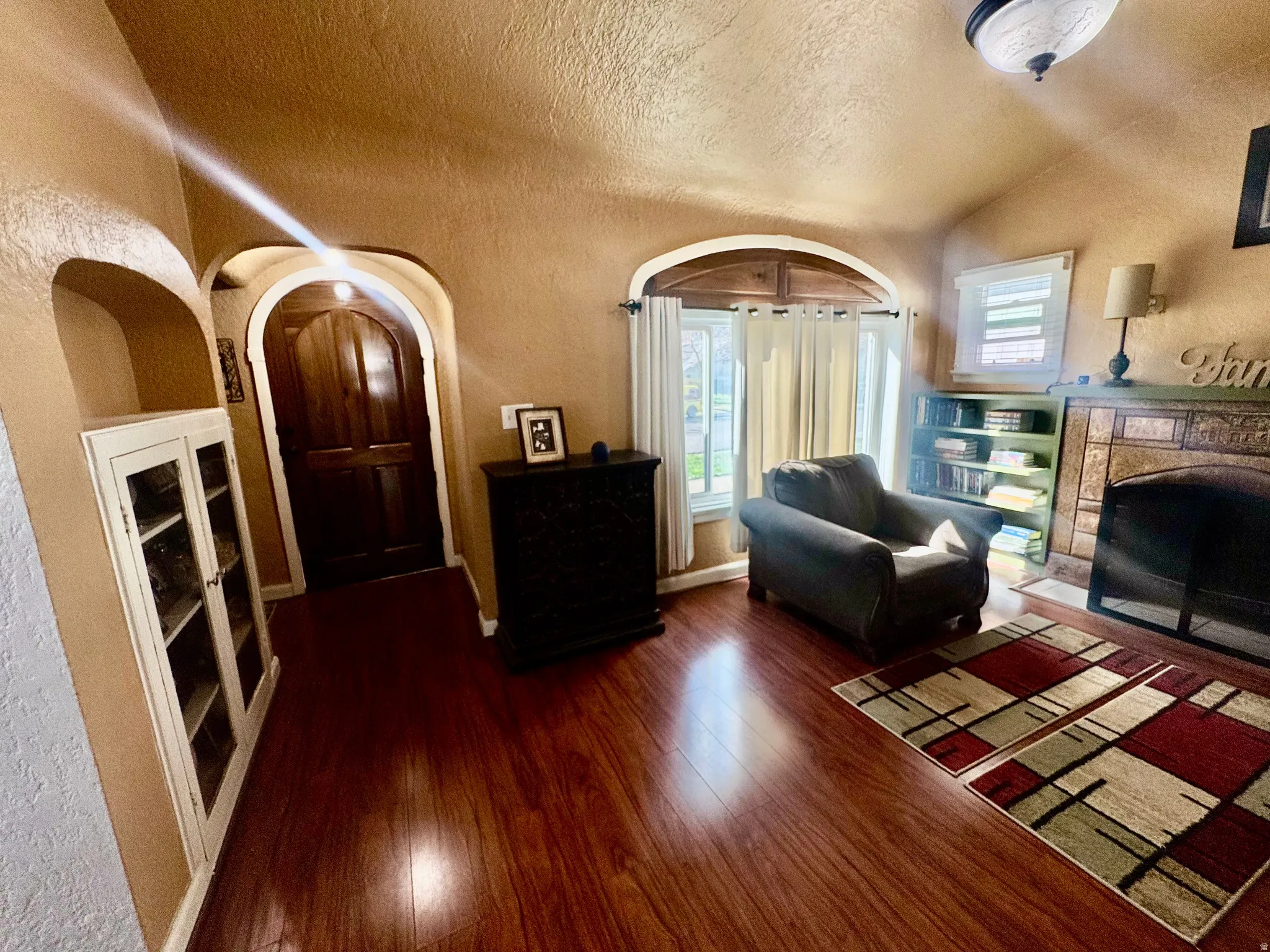 Living area featuring a textured wall, a fireplace, dark wood finished floors, built in features, and arched walkways