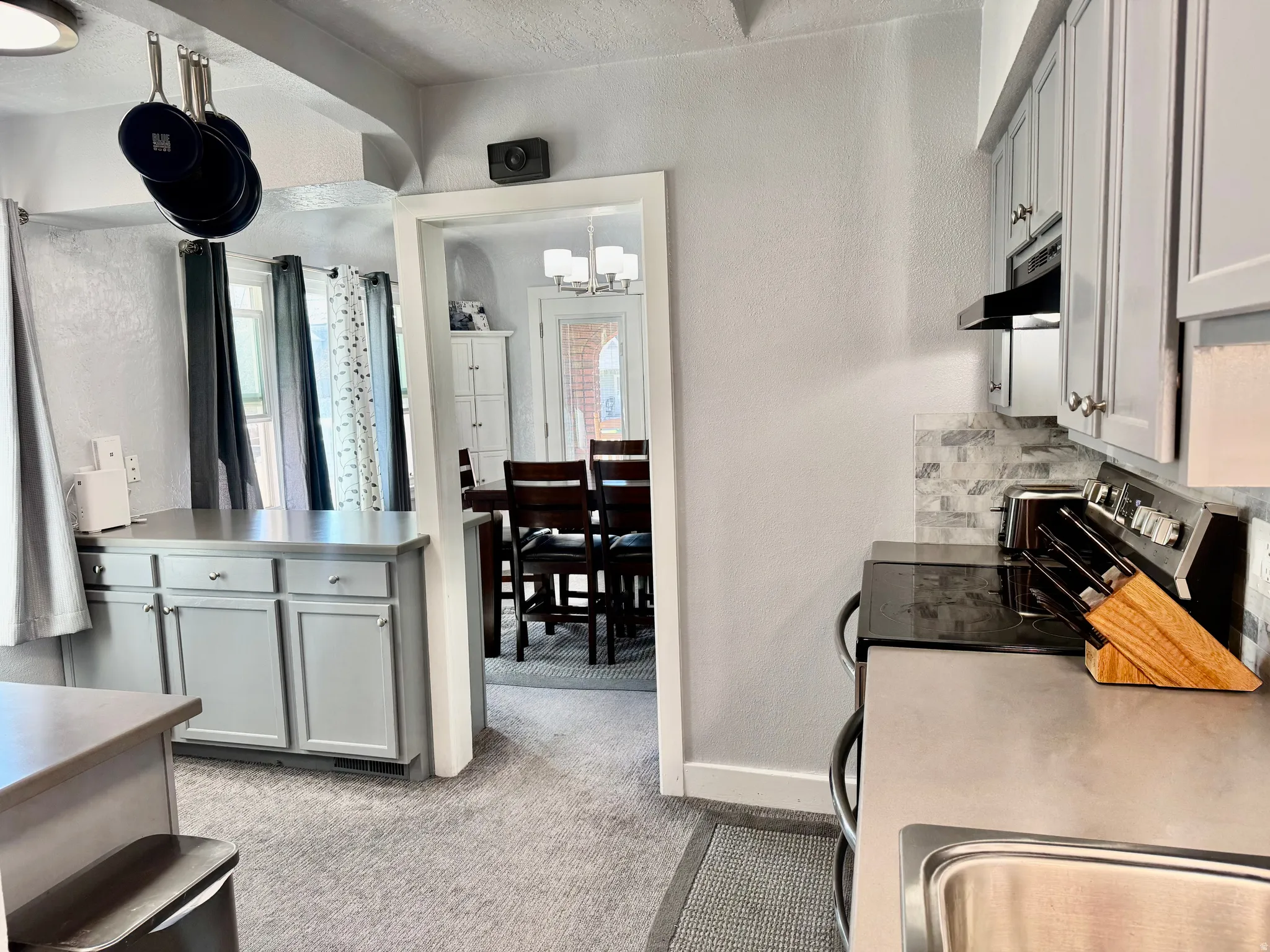 Kitchen with gray cabinetry, a textured wall, light countertops, light carpet, and stainless steel range with electric stovetop