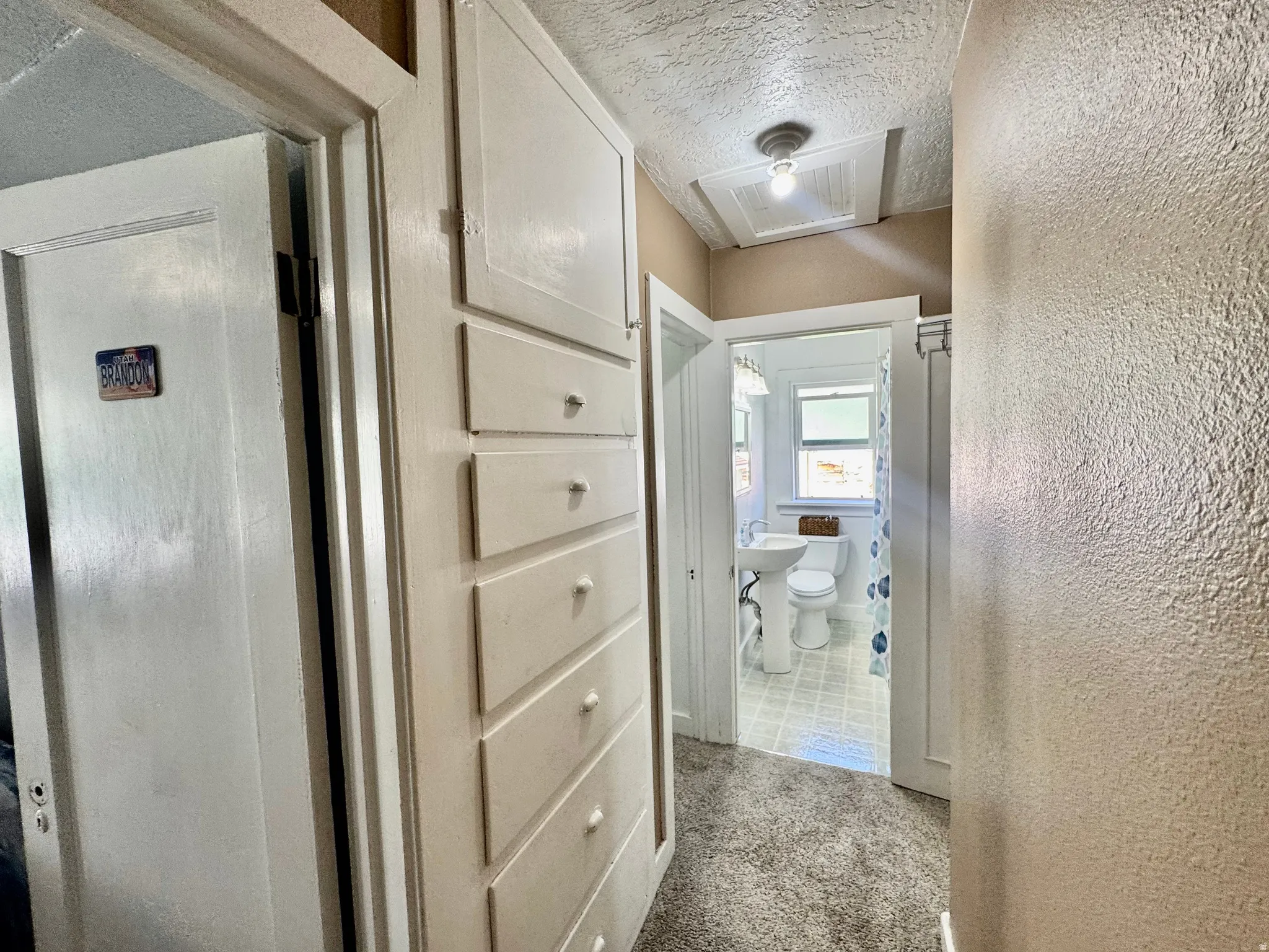 Hallway with a textured ceiling, a textured wall, and light carpet