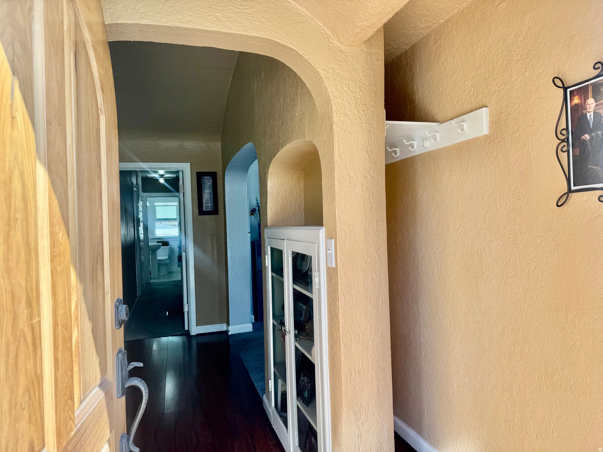 Corridor with a textured wall, dark wood-type flooring, and arched walkways