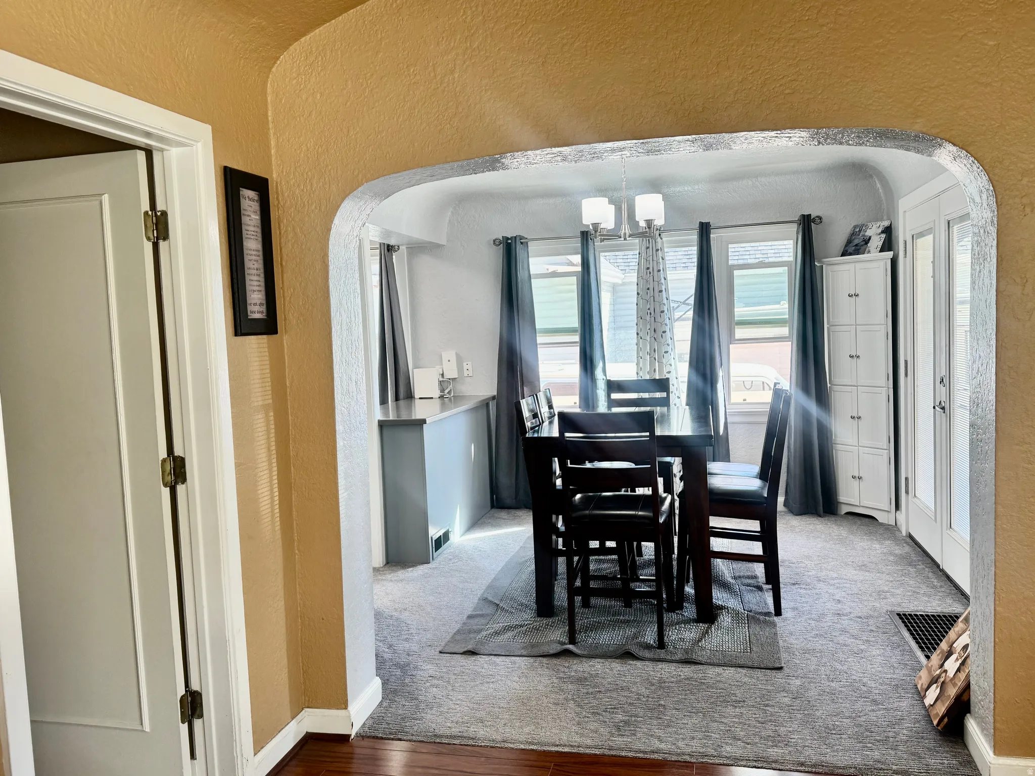Carpeted dining space with arched walkways, a textured wall, and hanging lights