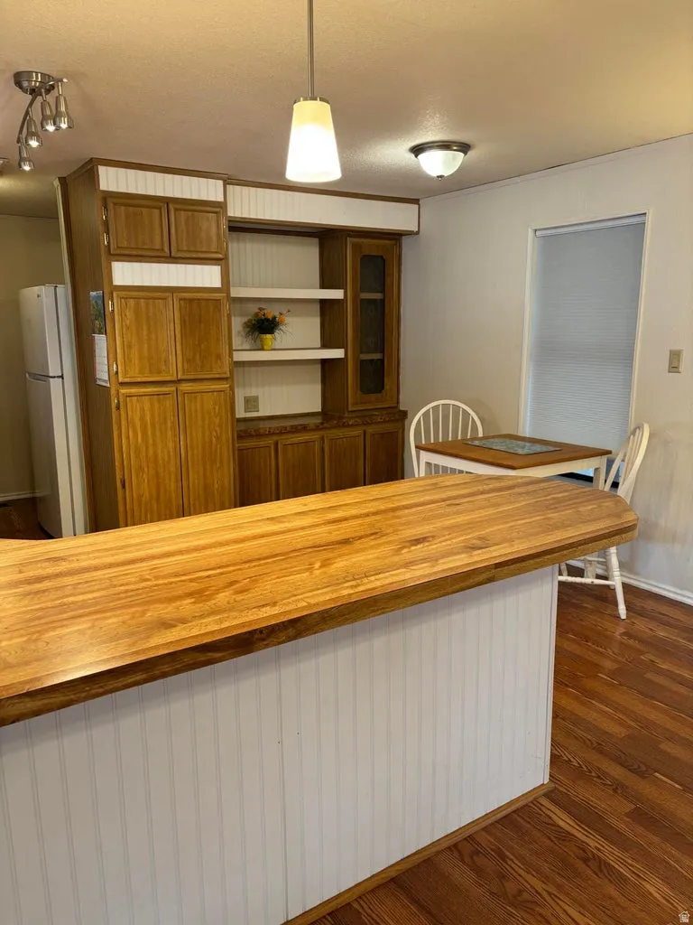 Kitchen featuring wood finish cabinets, decorative light fixtures, dark wood-type flooring, and freestanding refrigerator