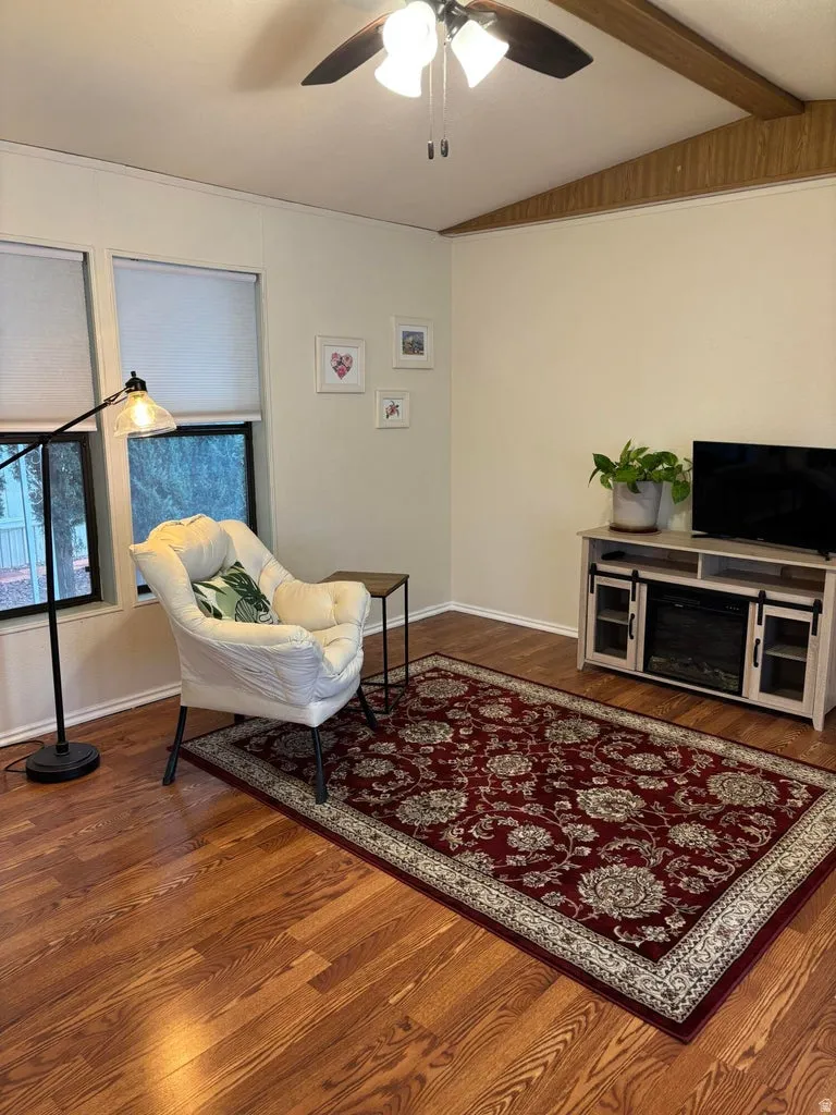 Sitting room with ceiling fan, vaulted ceiling with beams, and dark wood-style floors