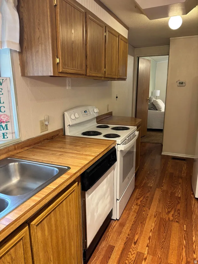 Kitchen with white electric stove, dark wood-type flooring, dishwasher, light countertops, and wood finish cabinets