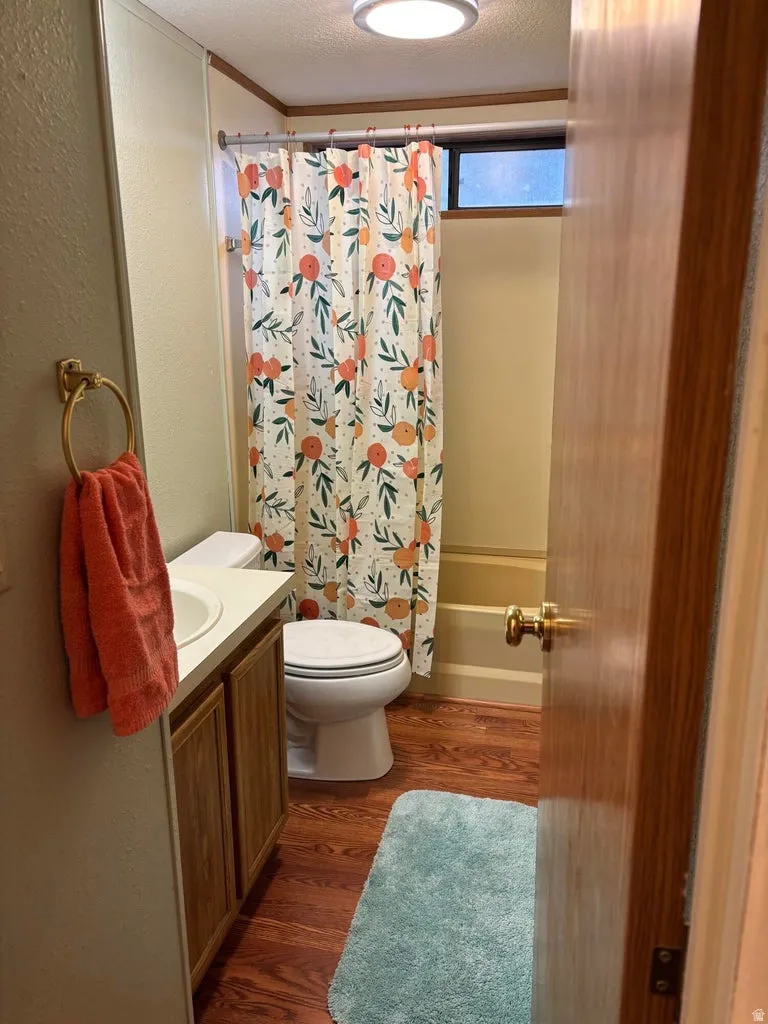 Full bath featuring vanity, dark wood-style floors, a textured wall, a textured ceiling, and shower / bathtub combination with curtain