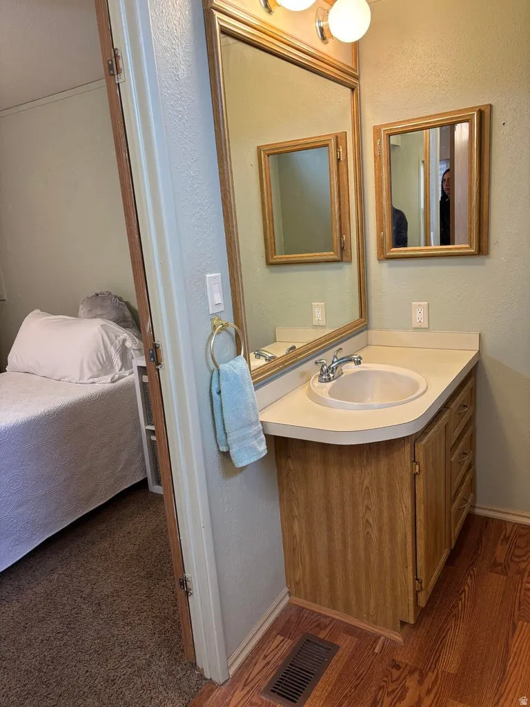 Bathroom featuring a textured wall, vanity, ensuite bathroom, and dark wood-style flooring