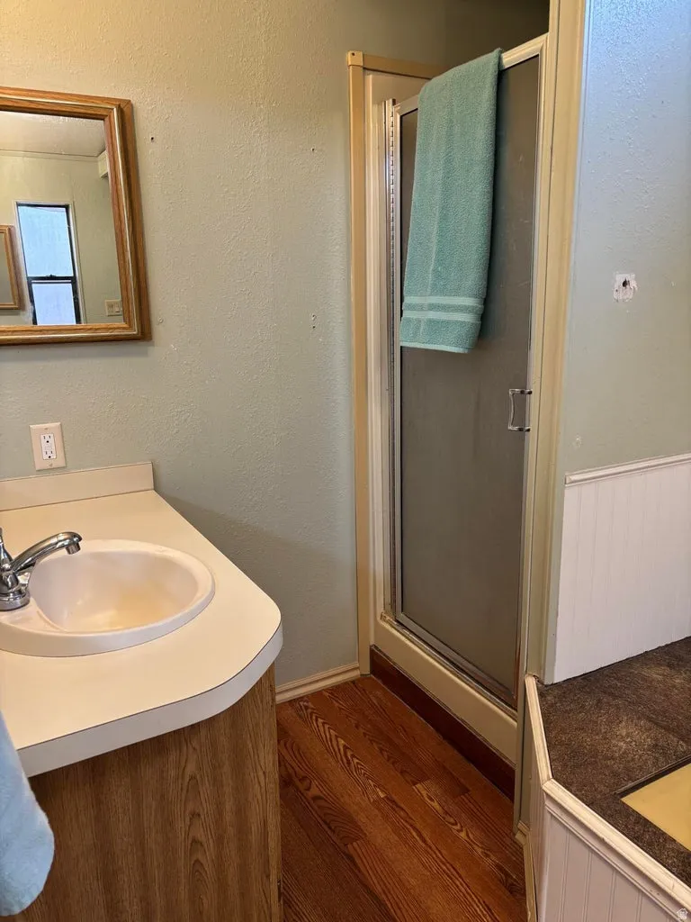 Full bathroom featuring vanity, a textured wall, a stall shower, and dark wood-type flooring