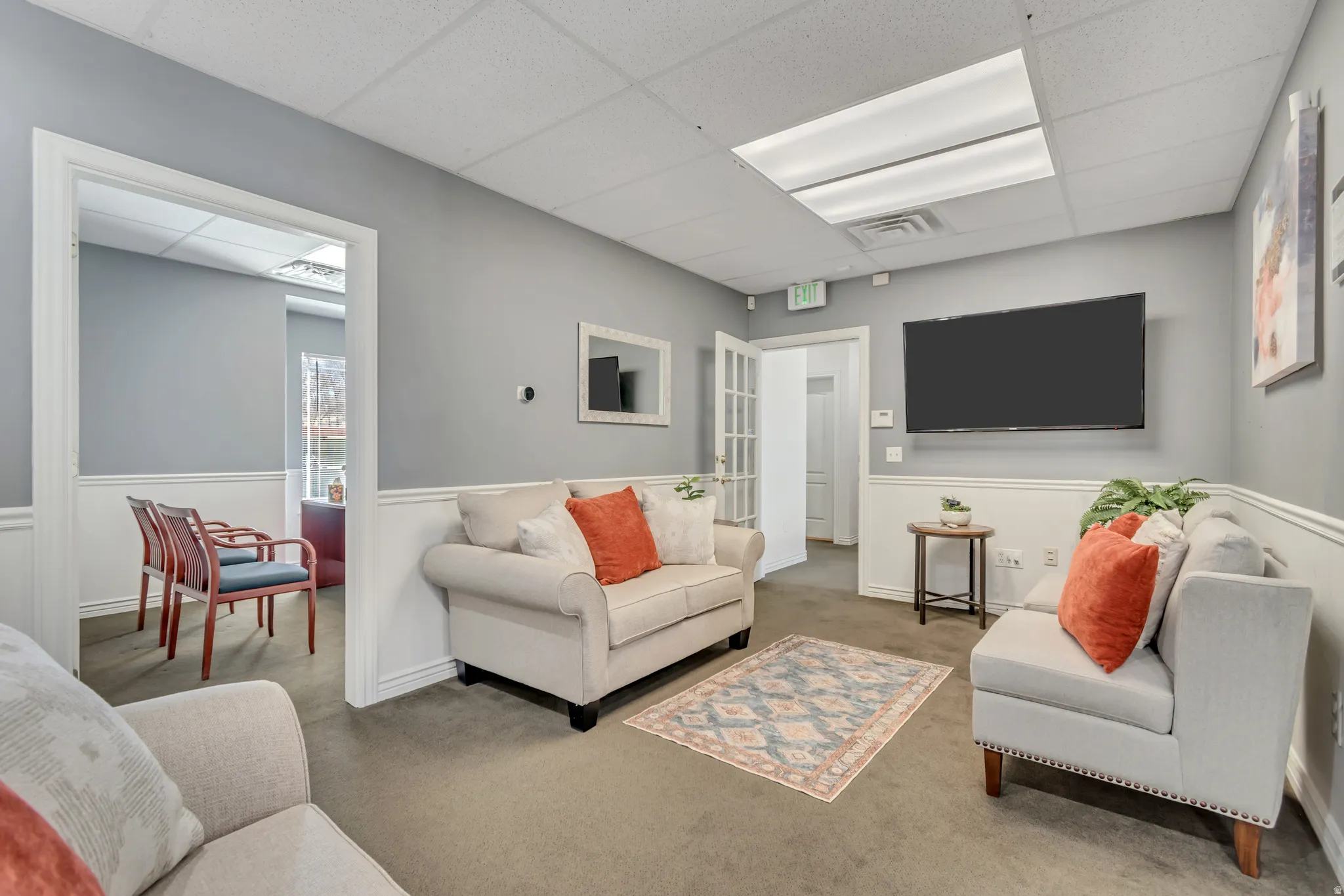 Living room featuring a paneled ceiling, carpet flooring, and a wainscoted wall