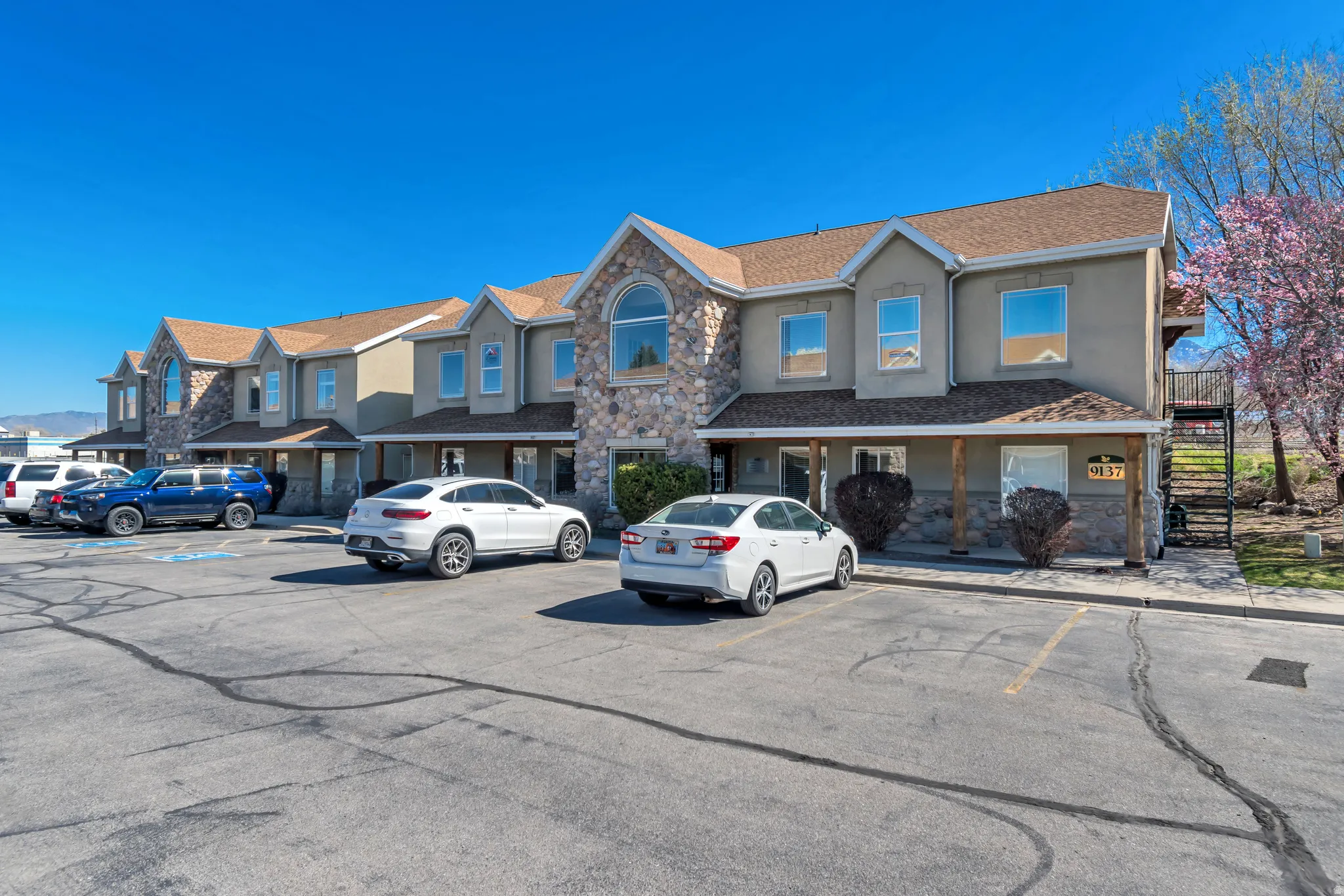 View of front facade with stone siding, stucco siding, uncovered parking, and roof with shingles