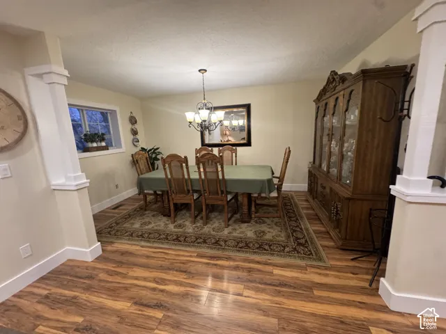Dining area with ornate columns, wood finished floors, hanging lights, and a textured ceiling