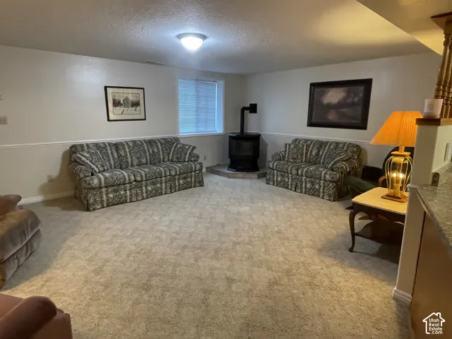 Spacious room featuring neutral carpeting and a black wood-burning stove on a stone-look hearth
