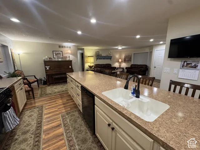 Kitchen featuring open floor plan, dark wood-style floors, black appliances, light stone counters, and recessed lighting