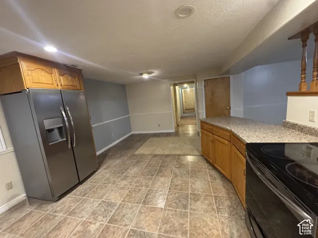 Kitchen with stainless steel refrigerator with ice dispenser, wood finish cabinets, black range with electric cooktop, stone finish floors, and recessed lighting