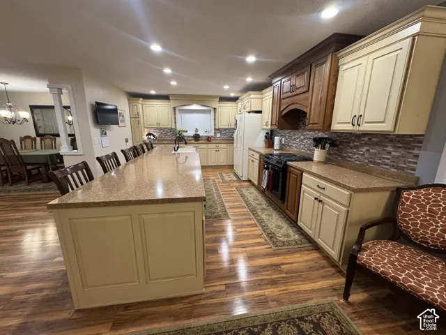 Kitchen with cream cabinets, a kitchen breakfast bar, dark wood-style floors, a large island with sink, and black range with gas stovetop