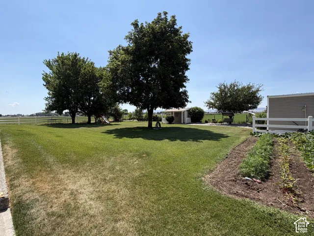 Expansive lawn area with mature trees, white fencing, and an established garden plot