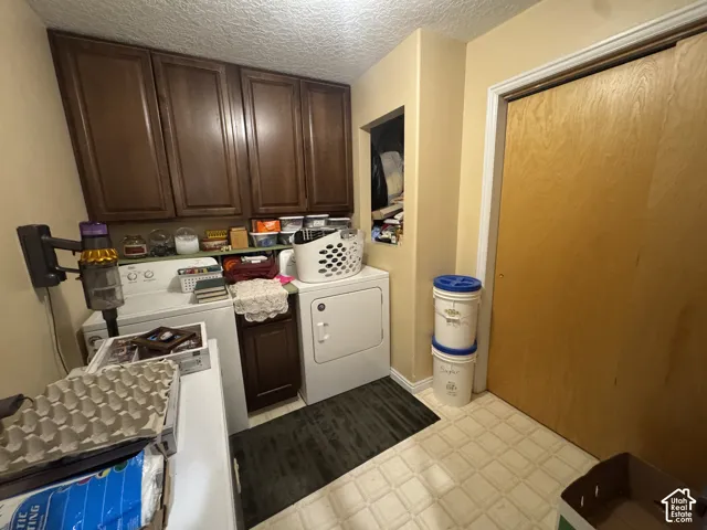Laundry room with light floors, cabinet space, a textured ceiling, and washing machine and clothes dryer