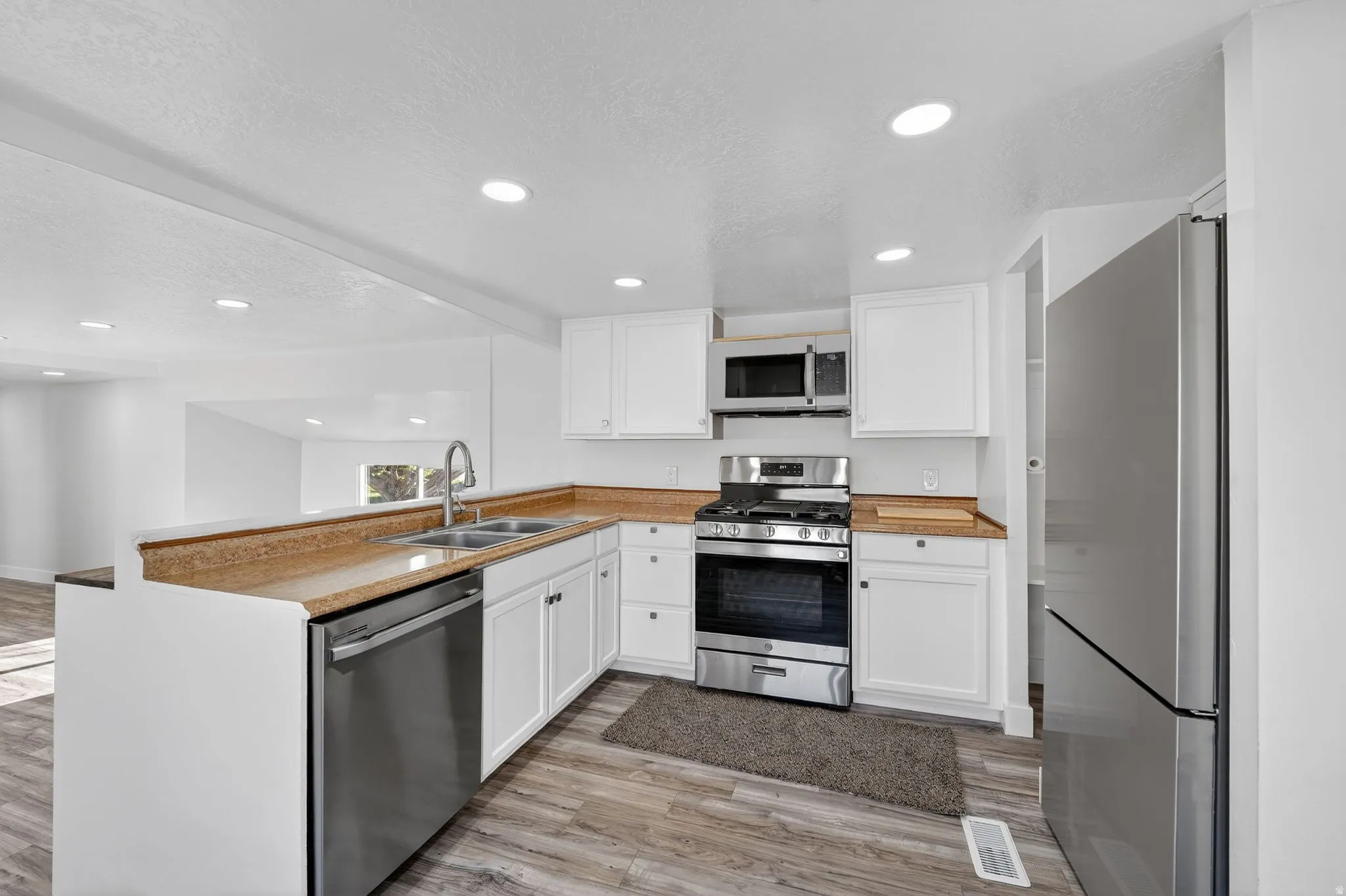 UPDATED Kitchen with white cabinets, stainless steel appliances, a textured ceiling, a peninsula, and recessed lighting