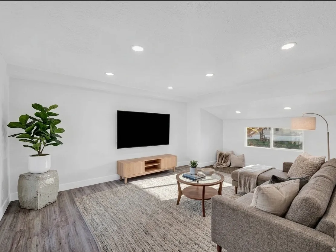 Spacious living area featuring light wood-finish flooring, recessed lighting, white walls, and bright window openings. Virtual stage