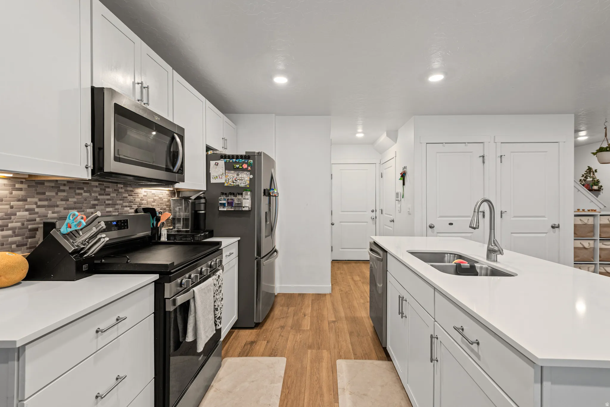 Kitchen with stainless steel appliances, a center island with sink, light wood-type flooring, white cabinets, and tasteful backsplash