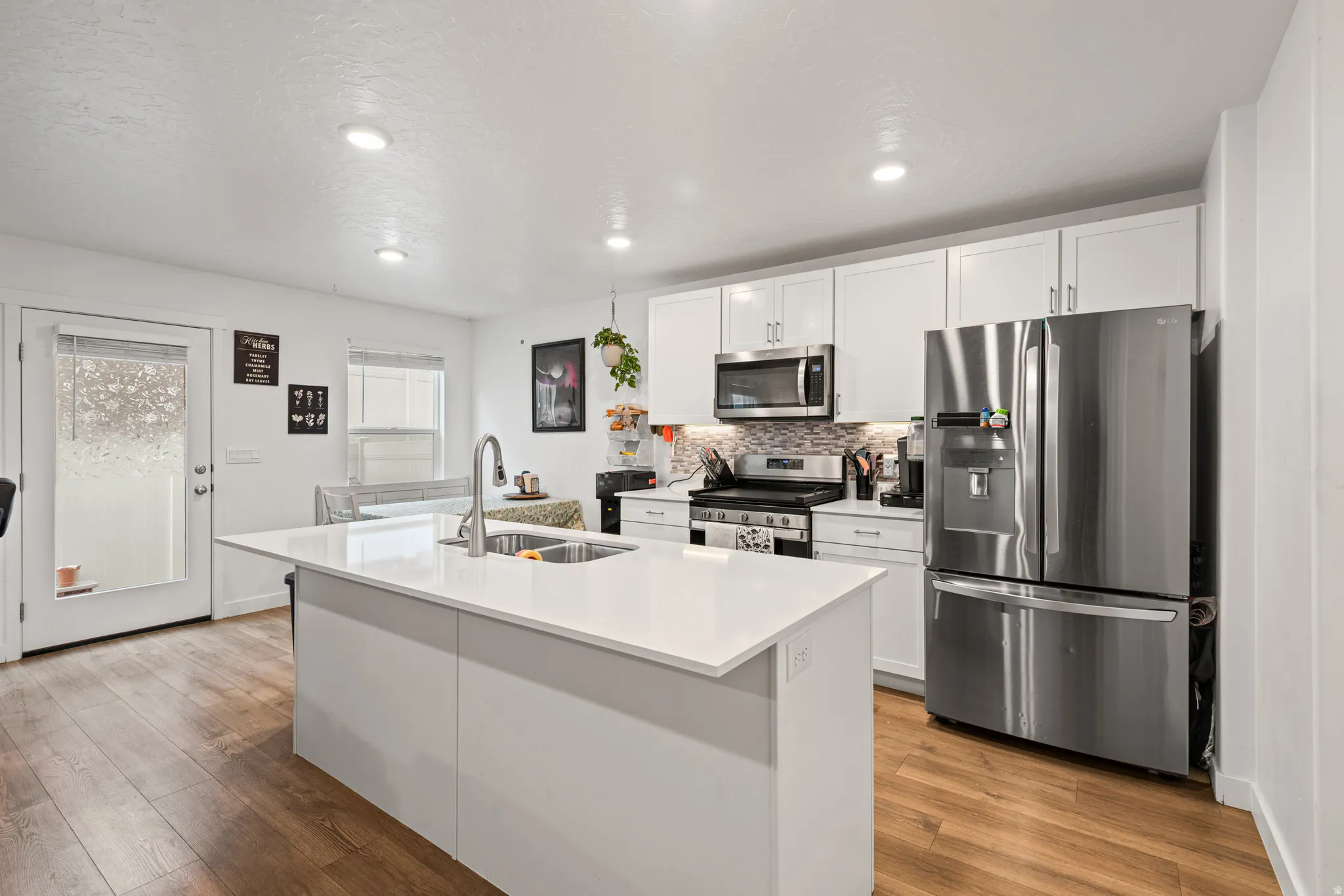 Kitchen featuring stainless steel appliances, white cabinetry, light wood-type flooring, a center island with sink, and recessed lighting