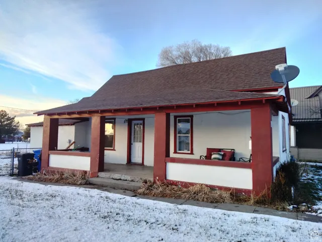View of front of property with a shingled roof, covered porch, and stucco siding