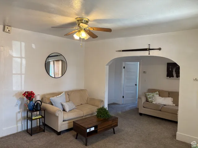 Living room with carpet floors, a ceiling fan, and arched walkways