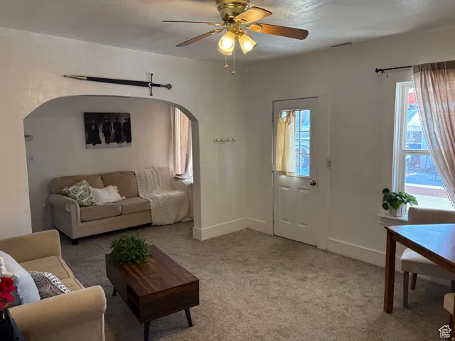 Living area with ceiling fan, light carpet, healthy amount of natural light, and arched walkways