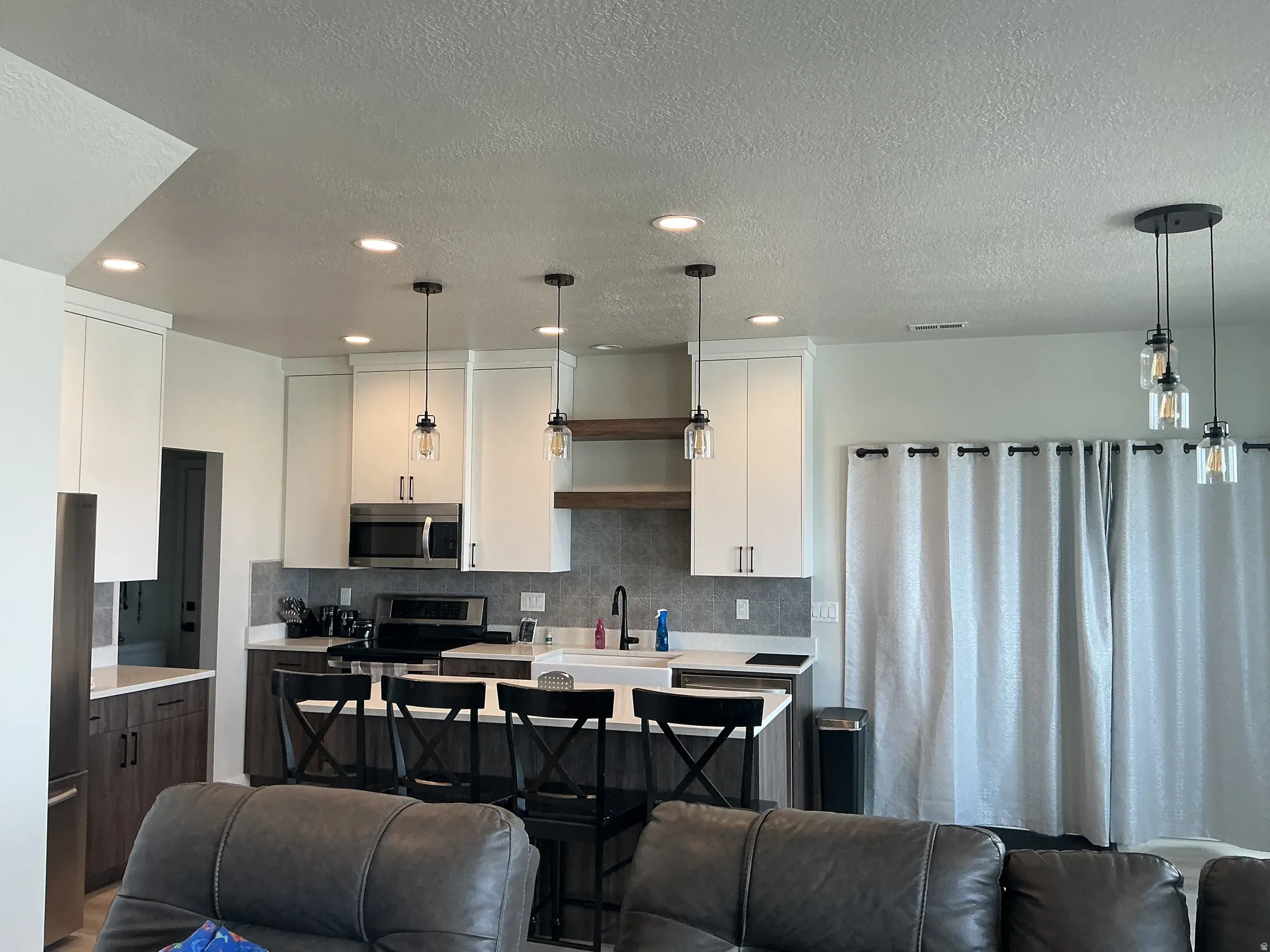 Kitchen featuring open floor plan, stainless steel appliances, a textured ceiling, decorative light fixtures, and two tone cabinets