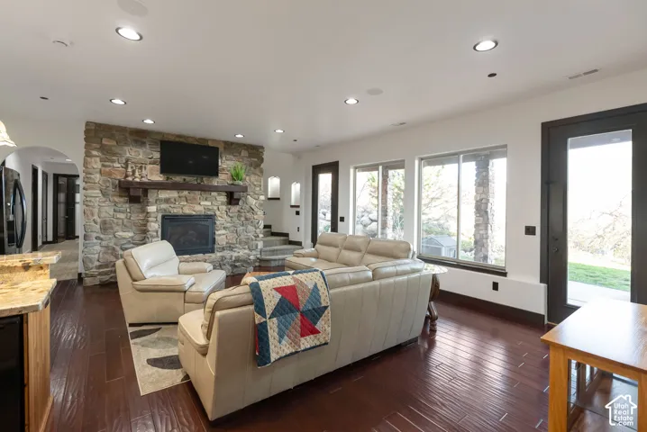 Living area featuring dark wood finished floors, a stone fireplace, recessed lighting, arched walkways, and wine cooler