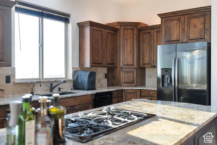 Kitchen with stainless steel fridge with ice dispenser, black gas cooktop, decorative backsplash, light stone counters, and dark wood finish cabinets