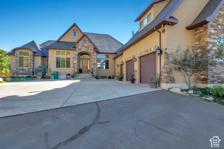 Stucco exterior with stone accents, arched entryway, multi-pane windows, and a two-car garage with carriage-style doors