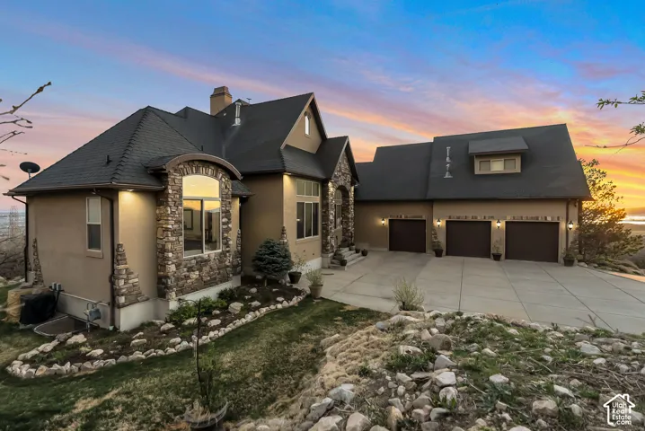 View of front facade featuring stucco siding, stone siding, concrete driveway, and a chimney