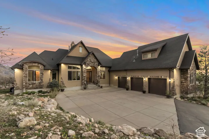 French country inspired facade with stone siding, an attached garage, concrete driveway, and a chimney