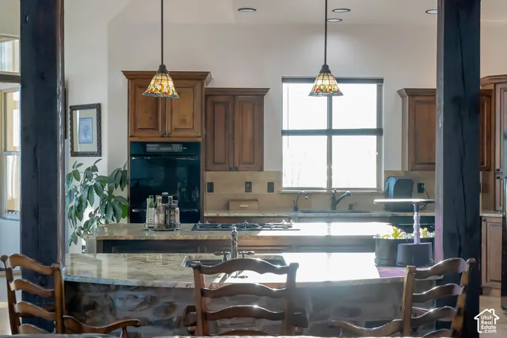 Kitchen with light stone countertops, decorative backsplash, hanging light fixtures, and a kitchen island with sink