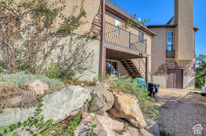 Exterior featuring stucco siding, stone accents, two-story structure, upper-level balcony with metal railing, and a ground-level patio door