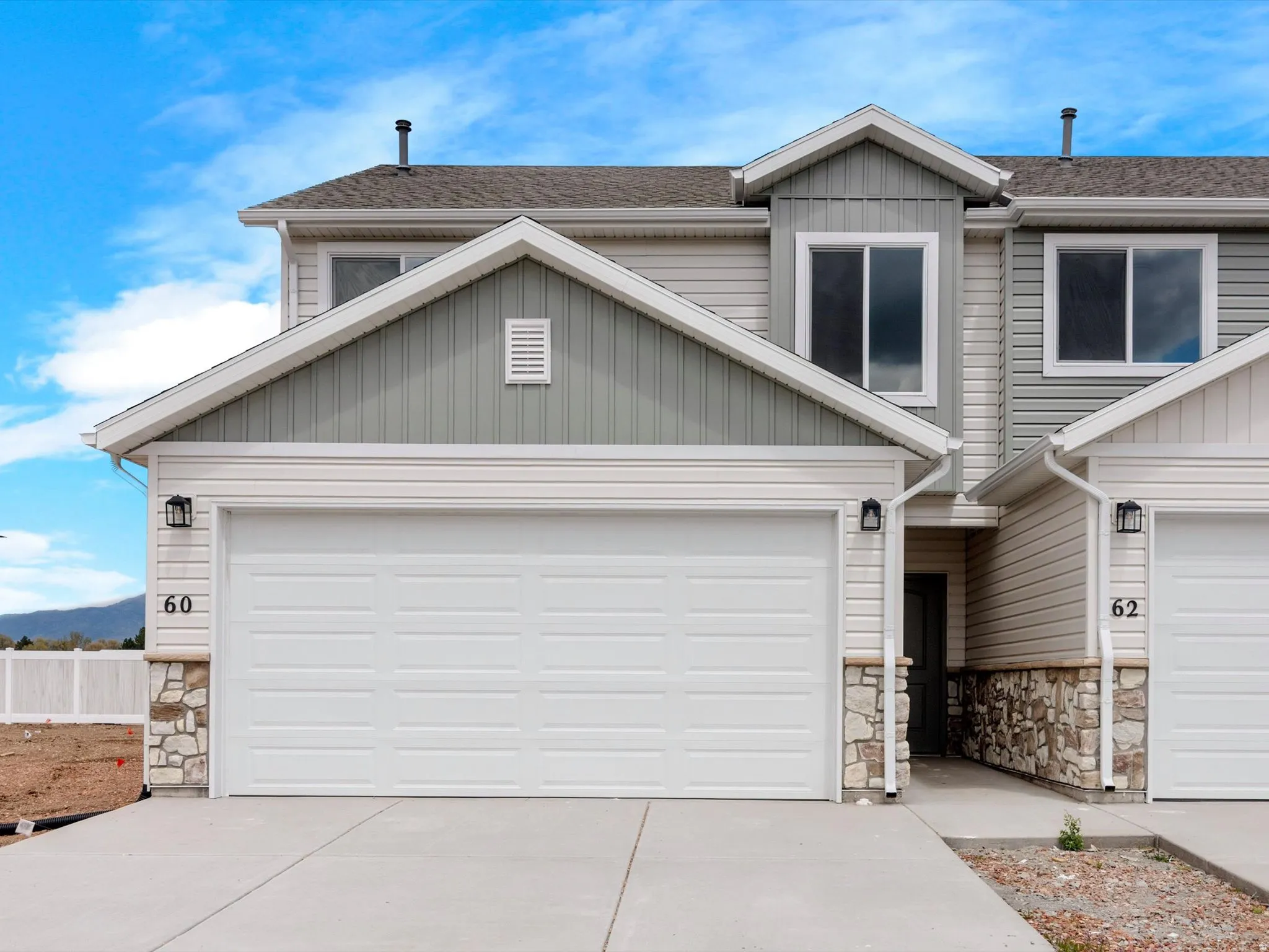 View of front of house with stone siding, roof with shingles, concrete driveway, and a garage