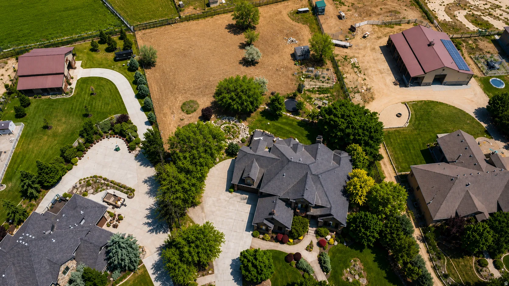 Expansive property featuring a large residence with a dark shingle roof, paved circular driveway, mature landscaping, and an additional barn-style structure with solar panels