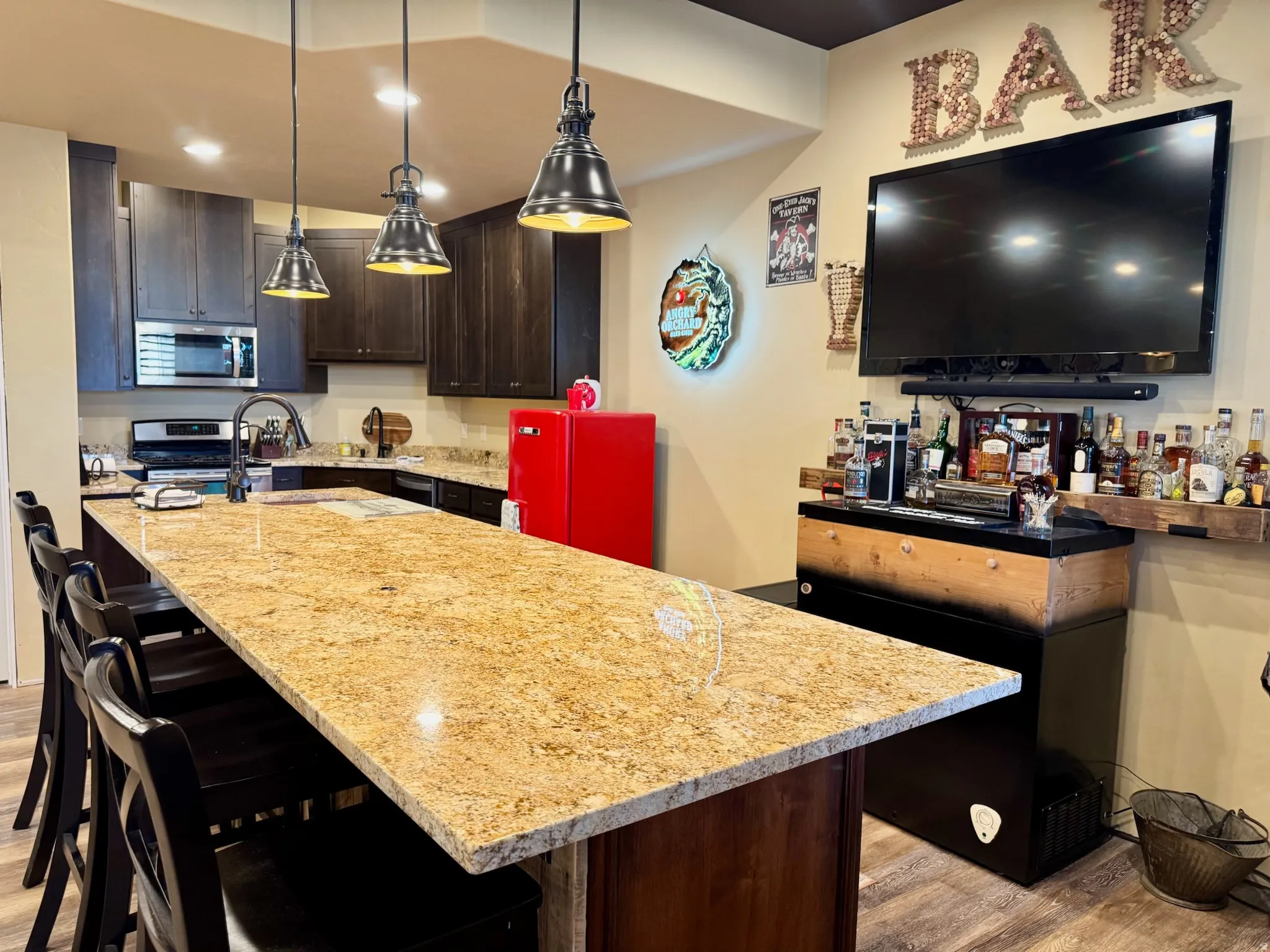 Kitchen featuring dark wood finish cabinetry, a kitchen island with sink, a breakfast bar area, and light stone counters