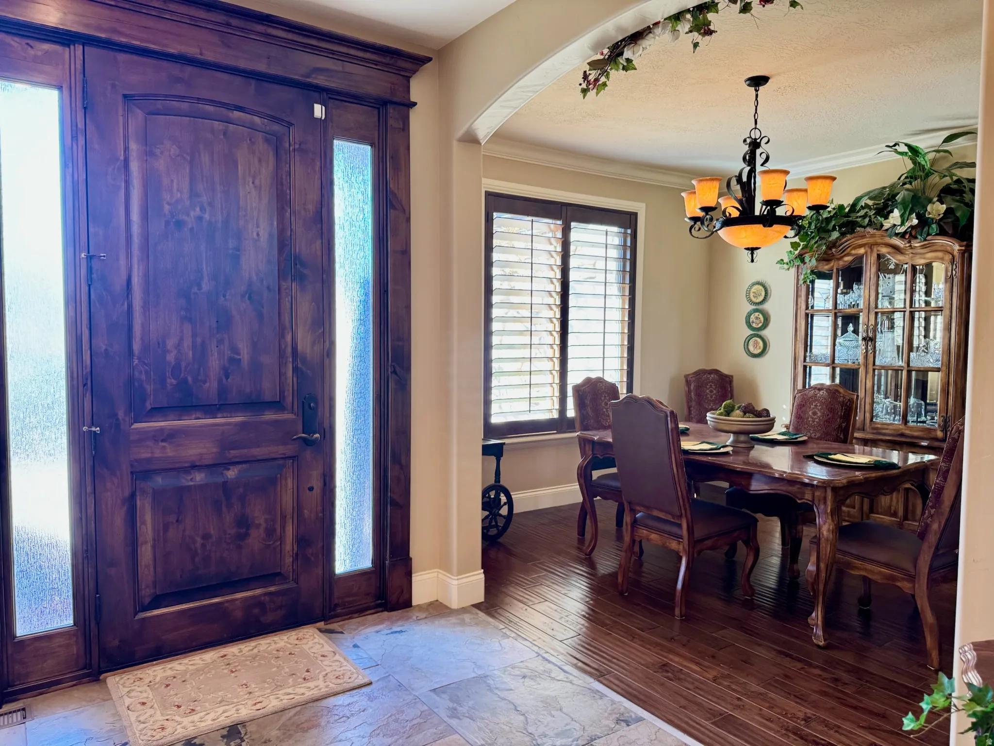 Foyer entrance featuring light wood finished floors, suspended lighting, crown molding, and arched walkways